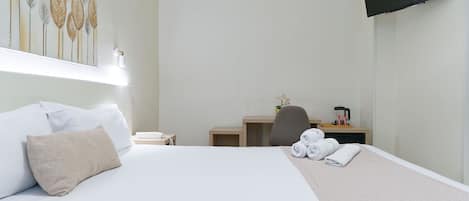 Ein Hotelzimmer mit Bett, Schreibtisch, Stuhl, Fernseher und einem Bild an der Wand.