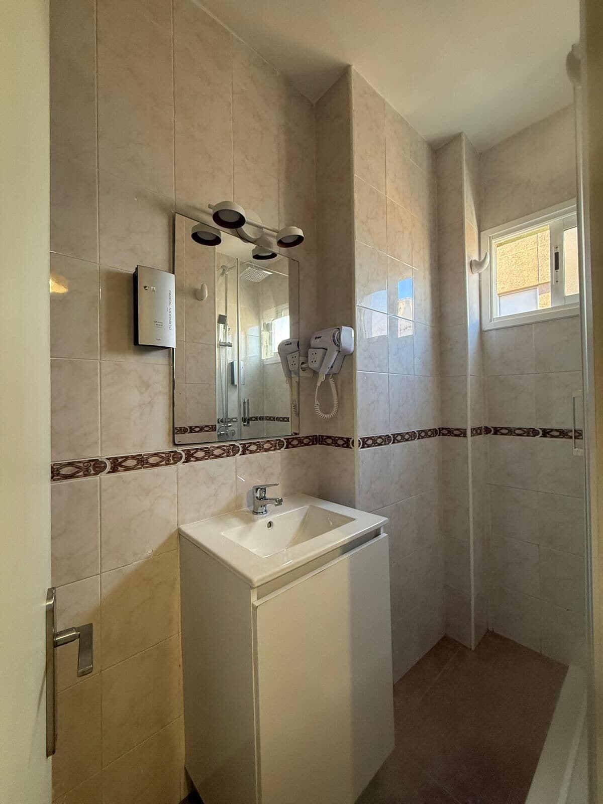A bathroom with a white sink, a mirror, and a hairdryer mounted on the wall.