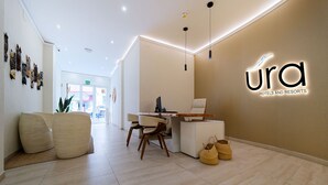 A modern hotel lobby with a reception desk, seating area, and a wall-mounted sign for 'Ura Hotels and Resorts'. - Ura Hotel Boutique Gurea (Las Palmas de Gran Canaria)