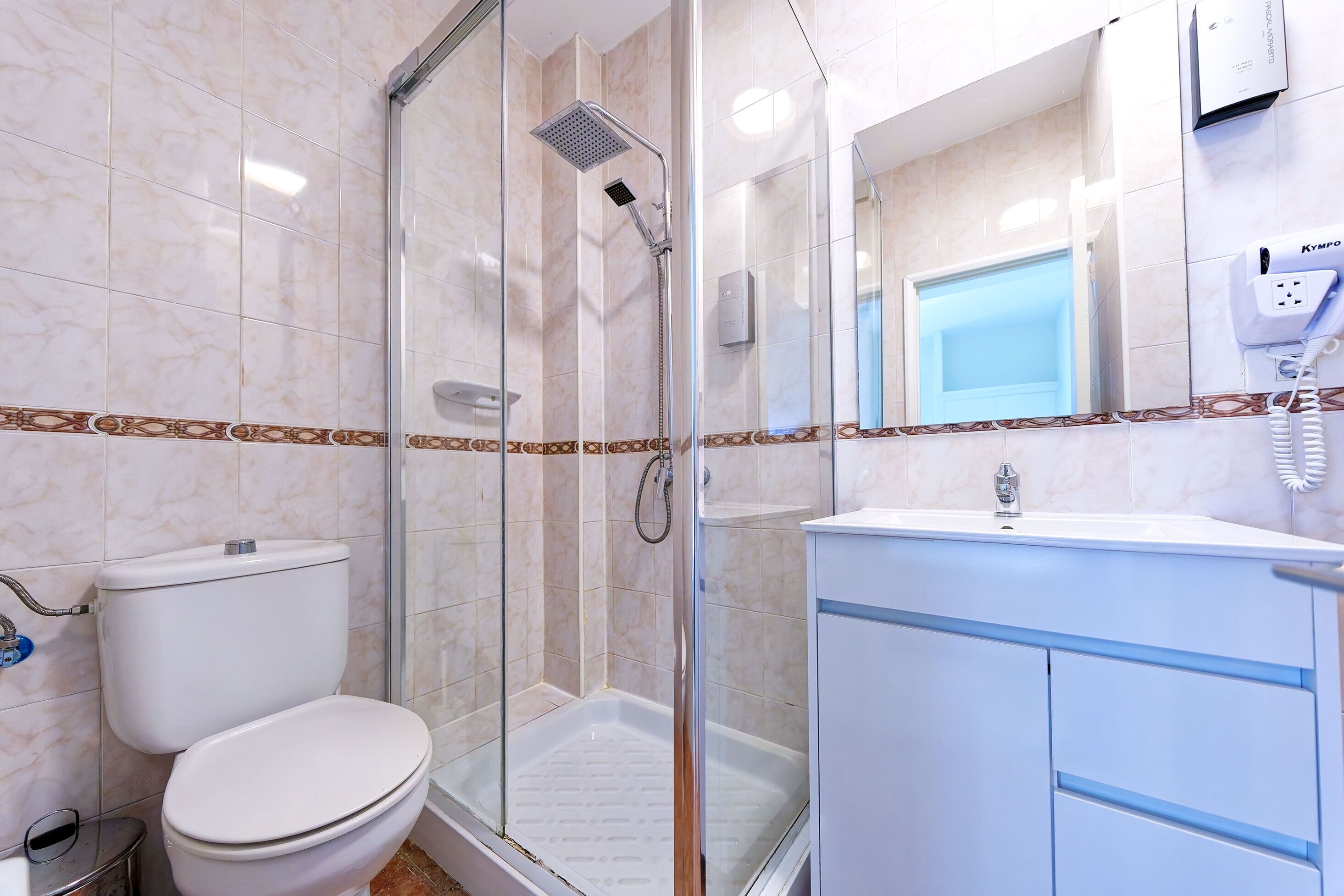 Un baño con inodoro, ducha con mampara de vidrio y lavamanos con espejo.