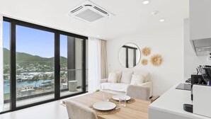 Habitación de hotel moderna con zona de comedor, sofá y un amplio ventanal con vistas a la ciudad y montañas.