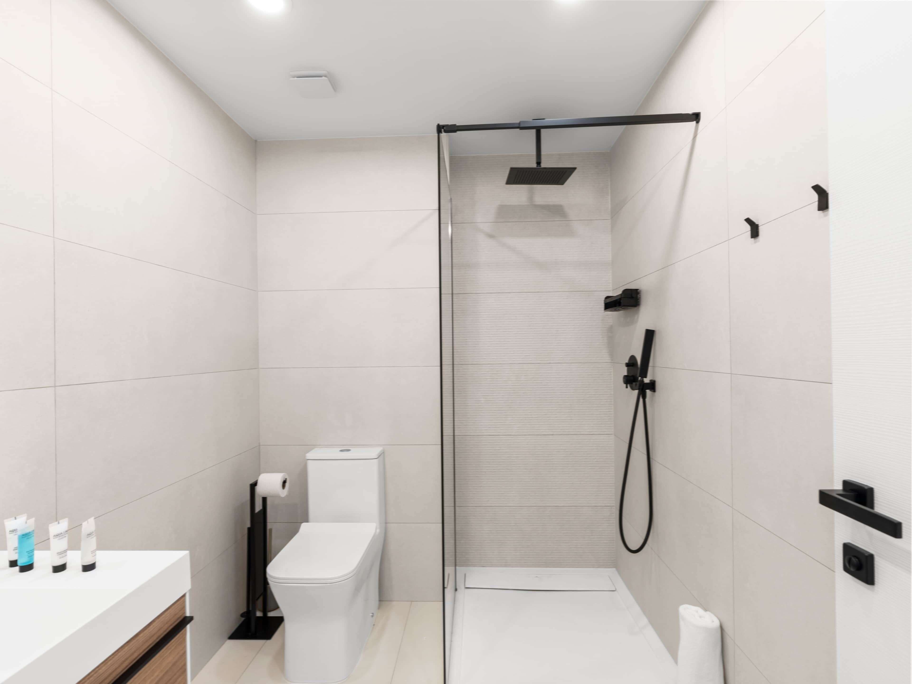A modern bathroom with a glass-enclosed shower, a toilet, and a sink with toiletries.