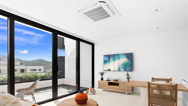 A modern living room with a sofa, a dining table, and a TV mounted on the wall.