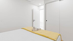 A bedroom with a bed, a yellow blanket, and a rolled towel.