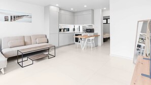 A modern, minimalist living room with a sofa, coffee table, and a dining area with a kitchen in the background.