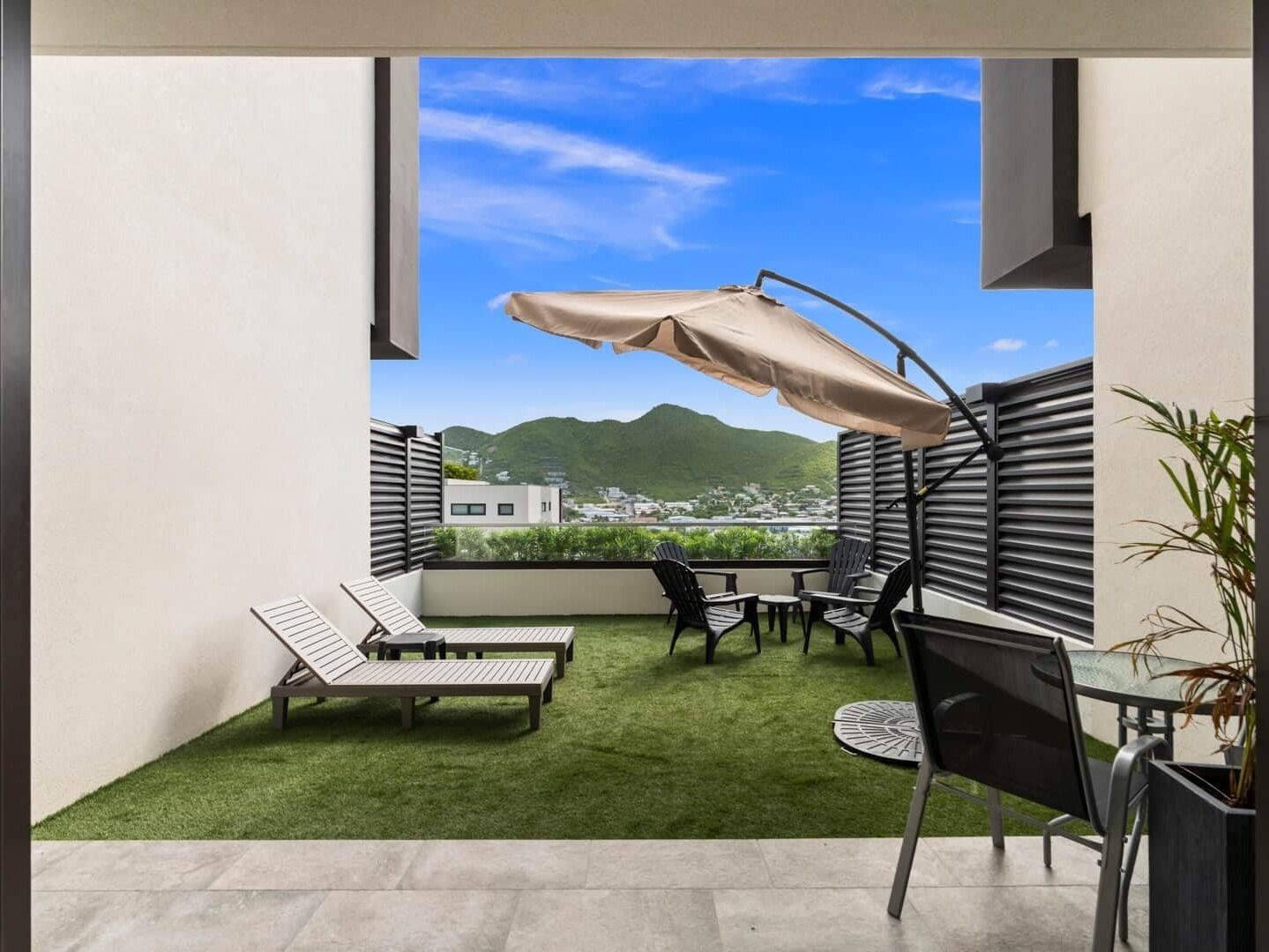 A balcony with a view of a mountain and a town, furnished with lounge chairs and a table.