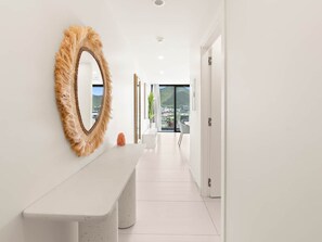 A modern hallway with a white bench, a large mirror with a textured frame, and a view of a cityscape through a glass door.