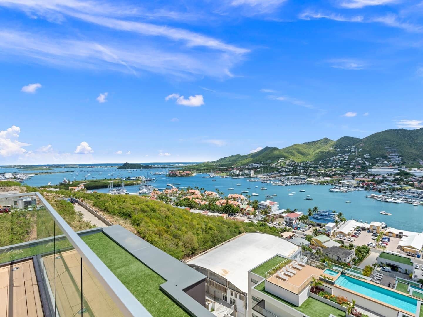 A coastal town with a marina, green hills in the background, and modern buildings with flat roofs.