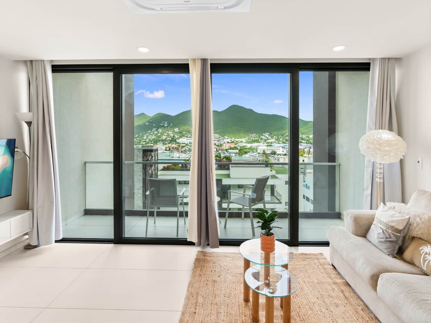 Una sala moderna con una mesa de vidrio, un sofá y vistas a un pueblo costero y montañas a través de amplios ventanales correderas.