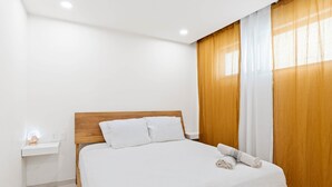 Un lit bien fait, avec une literie blanche, une tête de lit en bois et une table de chevet sur laquelle se trouve une lampe.