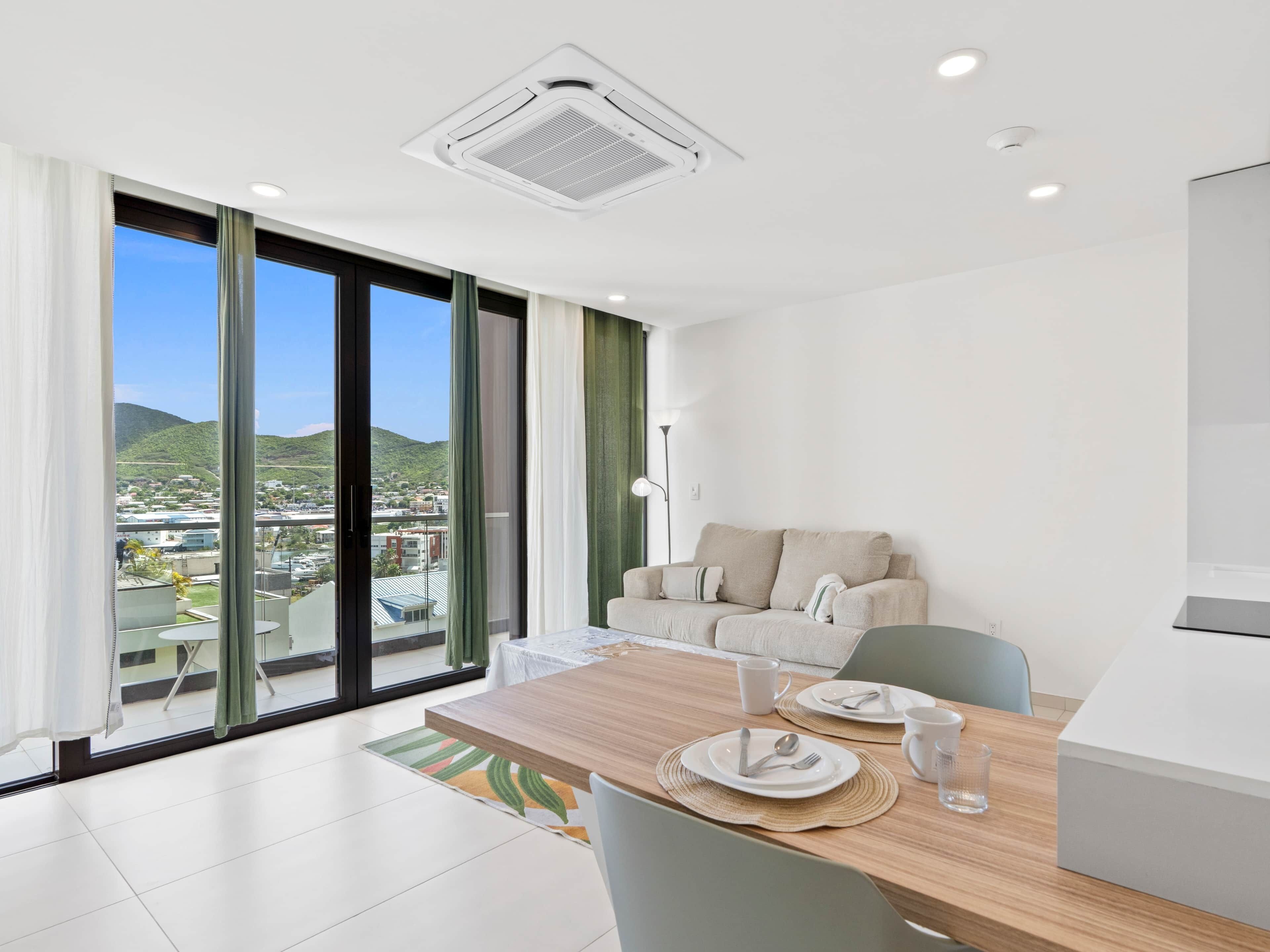 A modern hotel room with a dining area, a sofa, and a view of the cityscape.