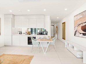 A modern kitchen with white cabinetry, a dining area with a light-colored table and chairs, and a large framed picture on the wall.