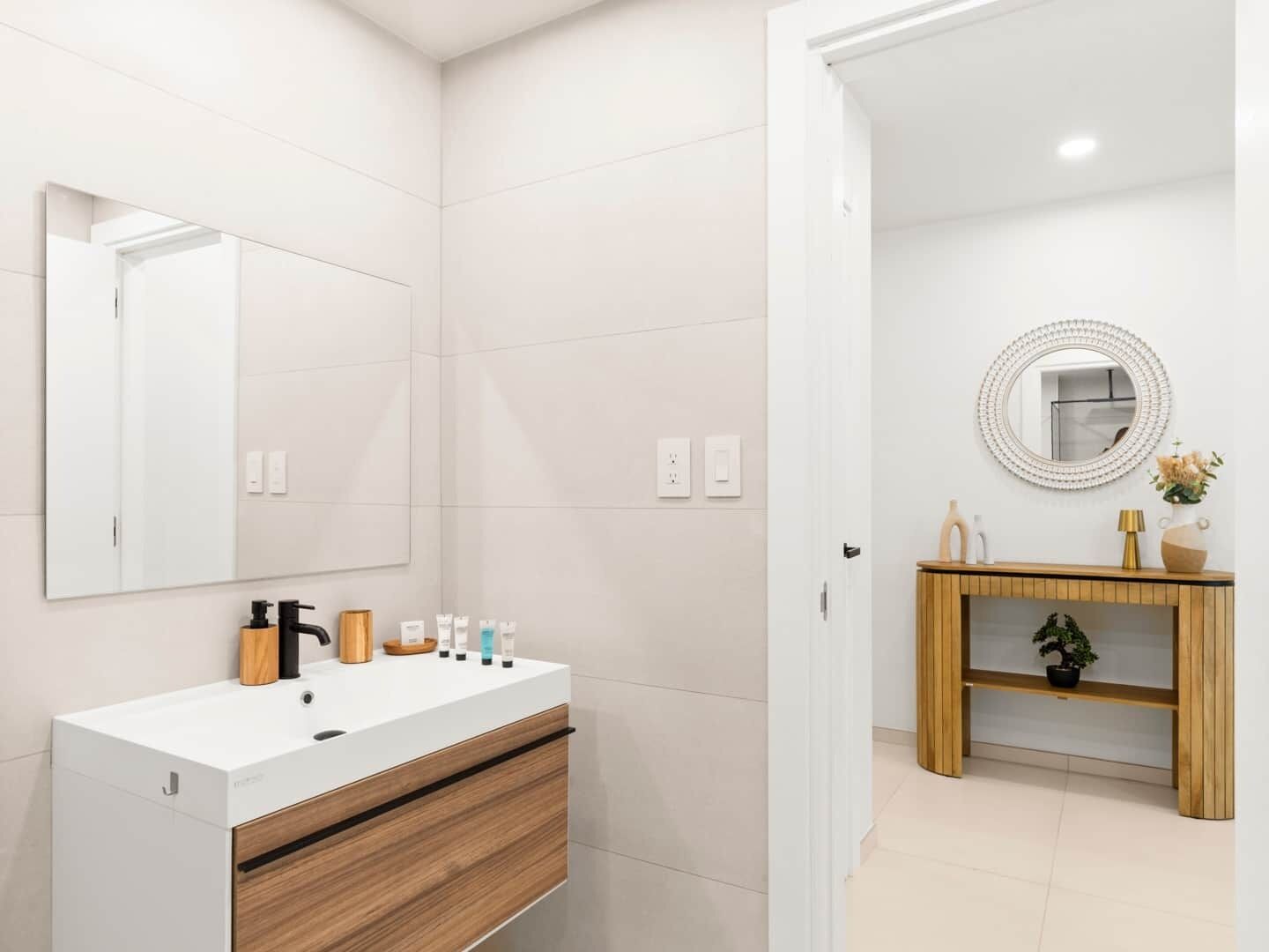 A modern bathroom with a white vanity, wooden drawer, and a round mirror above it.