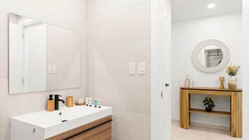 A modern bathroom with a white vanity, wooden drawer, and a round mirror above it.