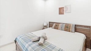 A neatly made bed with a plaid bedspread and a rolled towel, a wooden headboard, and a wall-mounted light fixture. - C333 - Charming Apartment with Lagoon View (Sint Maarten)