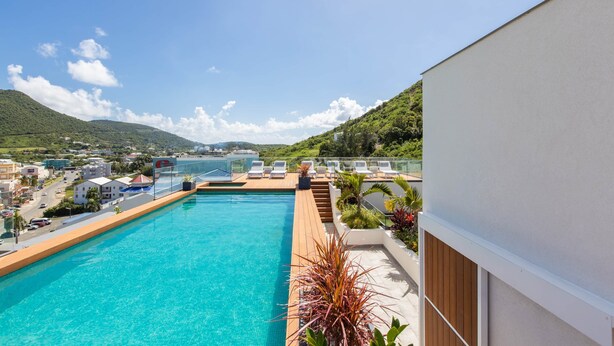 A rooftop pool with clear blue water, surrounded by lounge chairs and potted plants. - C333 - Charming Apartment with Lagoon View (Sint Maarten)