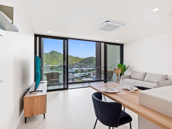 A modern room with a large window, a wooden desk, a black chair, a sofa, and a TV on a stand. - C314 - Stunning 1 Bedroom Apartment (Sint Maarten)