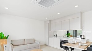 A modern kitchen with white cabinets, a dining table with chairs, a sofa, and a small round table.
