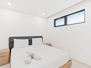 A modern bedroom with a bed, a nightstand, a window, and a wall socket. - C314 - Stunning 1 Bedroom Apartment (Sint Maarten)
