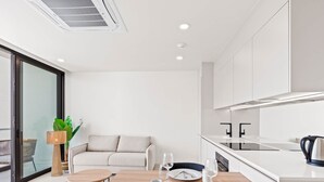 A modern kitchen with white cabinetry, a wooden dining table set with plates, cutlery, and glasses, and a sofa in the adjacent living area.