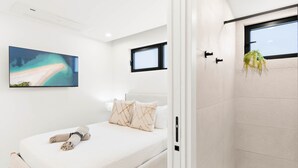 Een moderne slaapkamer met een bed, kussens, een schilderij en een douchehoek.