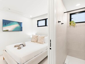 A modern bedroom with a bed, pillows, a painting, and a shower area.