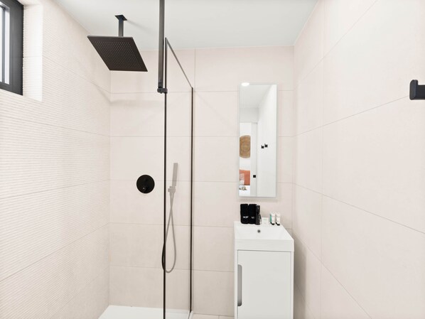 Une salle de bain moderne avec une douche à l’italienne, un lavabo blanc et un miroir au-dessus.