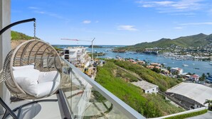 Een balkon met een rieten stoel, uitzicht op een jachthaven en een bouwplaats.