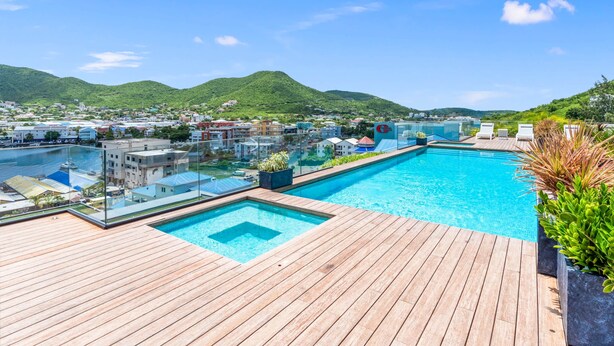 Une piscine sur le toit offrant une vue dégagée sur un port de plaisance et les collines environnantes.