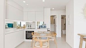 Een moderne keuken met witte kasten, een eettafel met vier stoelen en een magnetron.