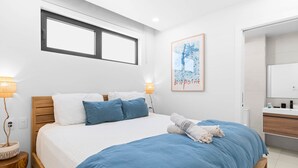Ein modernes Schlafzimmer mit einem großen Bett, einem hölzernen Kopfteil, einem Nachttisch mit Lampe und einem gerahmten Kunstwerk an der Wand.