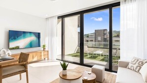 Un salon moderne doté d’une grande fenêtre, d’un téléviseur à écran plat, d’un bureau en bois et d’un canapé.