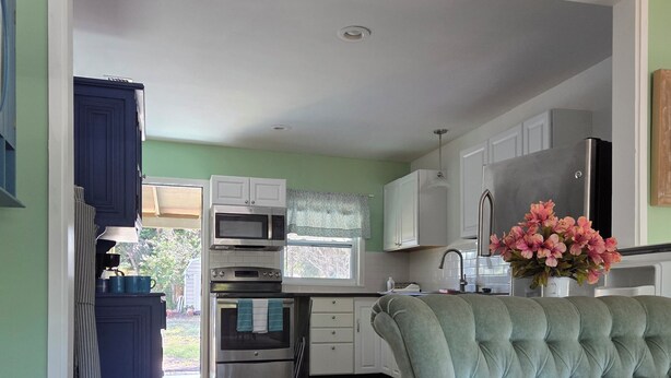 A spacious living room with a green sofa, a wooden coffee table, and a view into the kitchen area. - Cozy Cute Beachy 2-bedroom house with Backyard, Parking & grill (Clearwater)