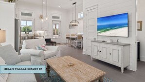 A spacious living room with a large TV, white furniture, and a view of the ocean. - Beach Village Resort BVR07 | by Liquid Life (Orange Beach)