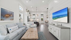 A spacious living room with a light gray sofa, a wooden coffee table, and a large flat-screen TV on the wall. - Beach Village Resort BVR07 | by Liquid Life (Orange Beach)