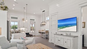 Amplia sala de estar con un televisor grande, muebles blancos y vista al océano.