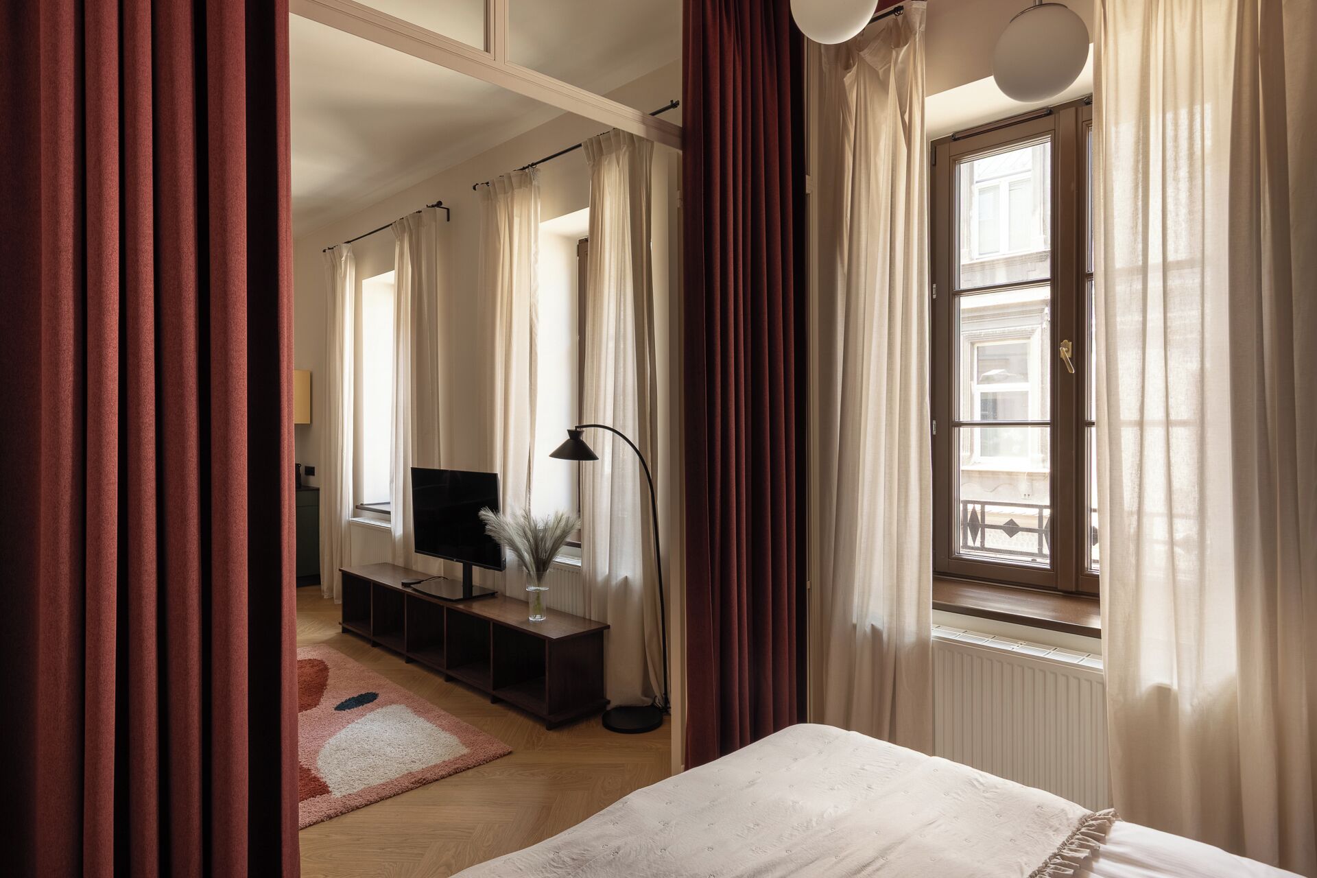 Quarto de hotel com cama, televisão, escrivaninha e janela com cortinas.