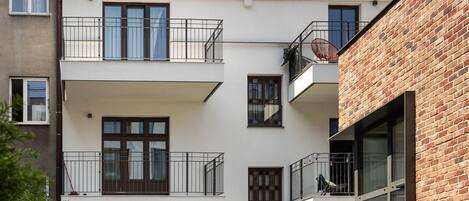 Un moderno edificio residencial de varios pisos con balcones, un sendero de madera y fachada de ladrillo.