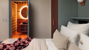 A bedroom with a bed, pillows, a bedside table, and a nightstand. There is a door leading to a bathroom with a mirror and a towel rack. - Soho Residence Kazimierz by Downtown Apartments (Kraków)