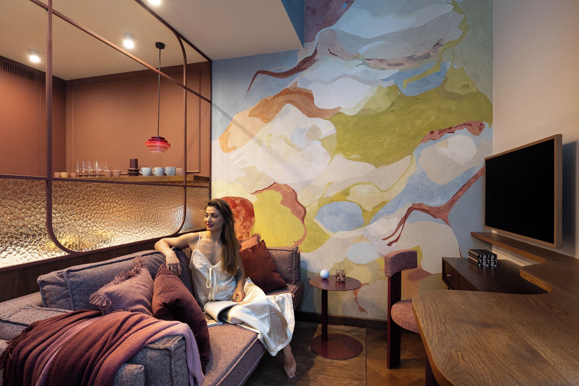 A modern living room with a large abstract painting, a sofa, a small round table, and a television.