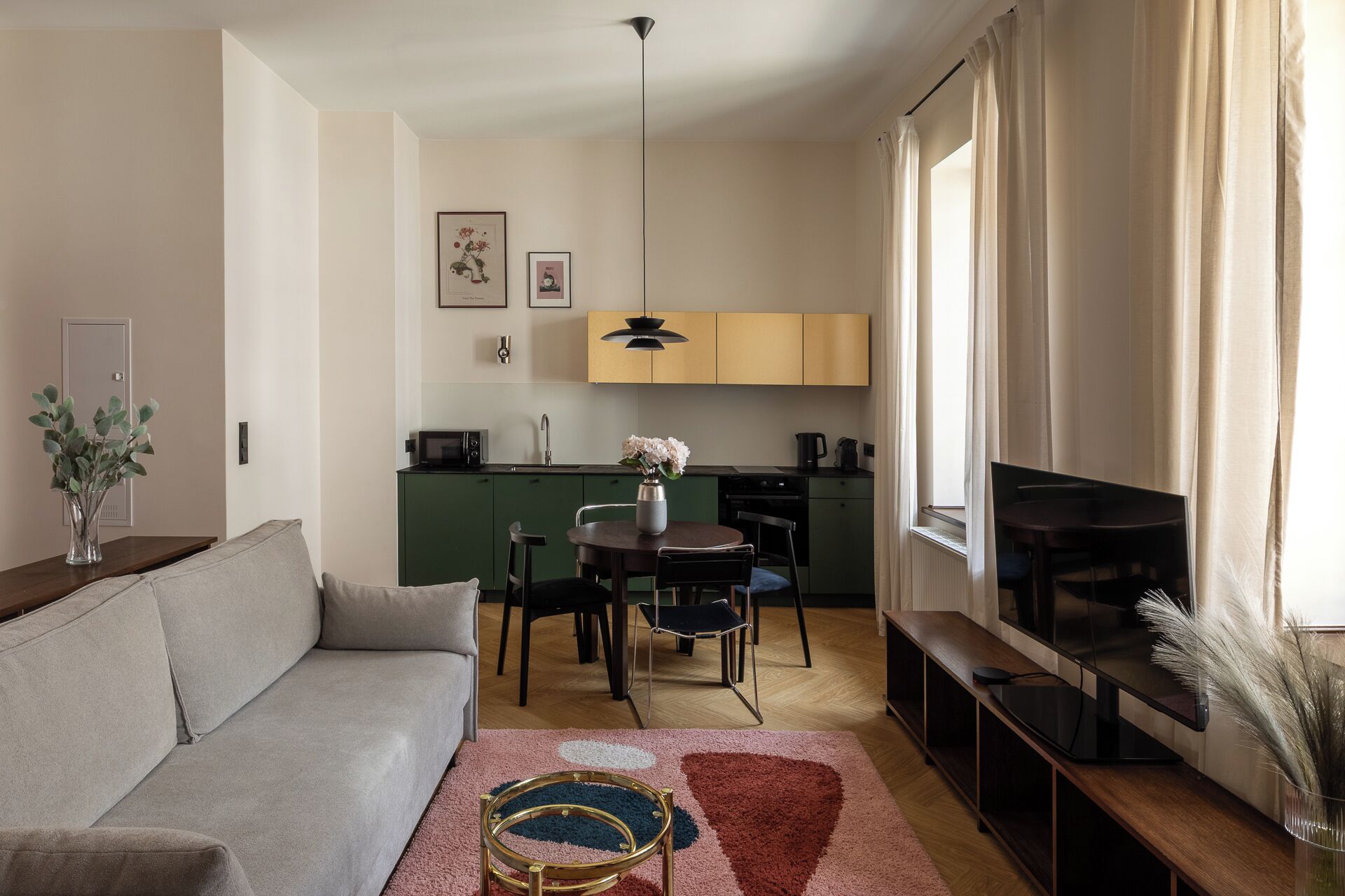 Ett kompakt bostadsutrymme med en soffa, ett matbord med stolar, en köksdel och en tv som står på ett TV-bord.