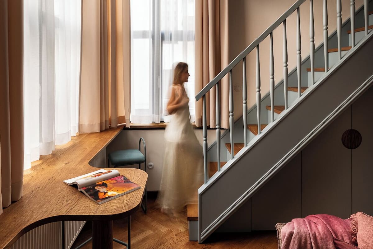 Un interior moderno con una escalera, un comedor con mesa y sillas, y un amplio ventanal con cortinas.