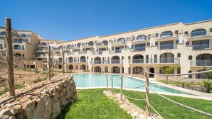 A hotel with multiple balconies, a swimming pool, and a stone wall. - Hal Wardija in Qala Gozo With Terrace Pool BBQ (Qala)