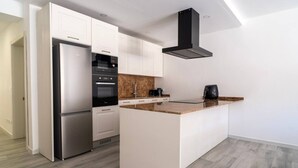 A modern kitchen with white cabinetry, a stainless steel refrigerator, a built-in oven, a coffee maker, and a black range hood. - Hal Wardija in Qala Gozo With Terrace Pool BBQ (Qala)