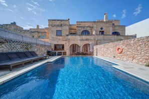 Una piscina con sillas de descanso y un muro de piedra.