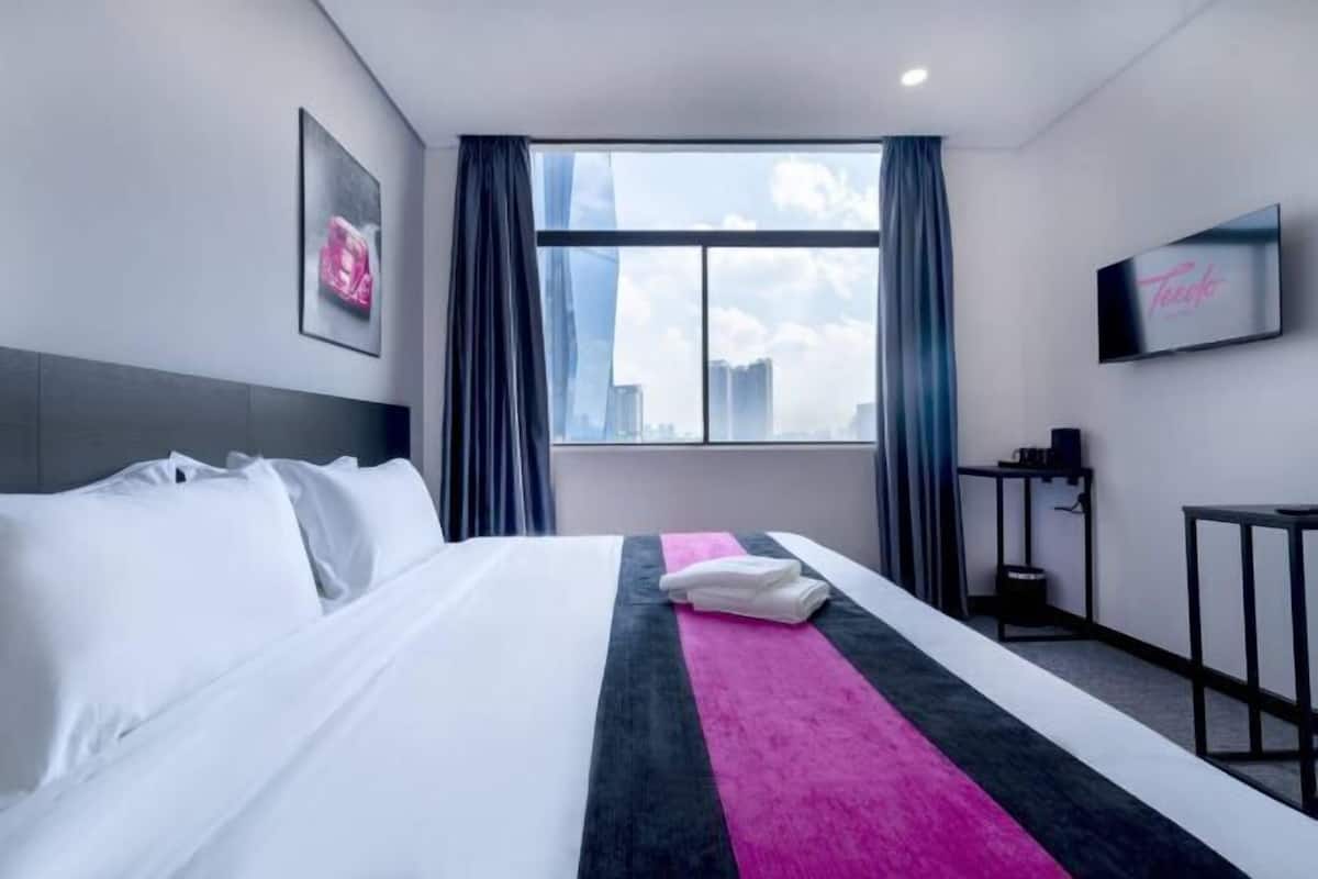 A hotel room with a large bed, a TV mounted on the wall, and a window with curtains.