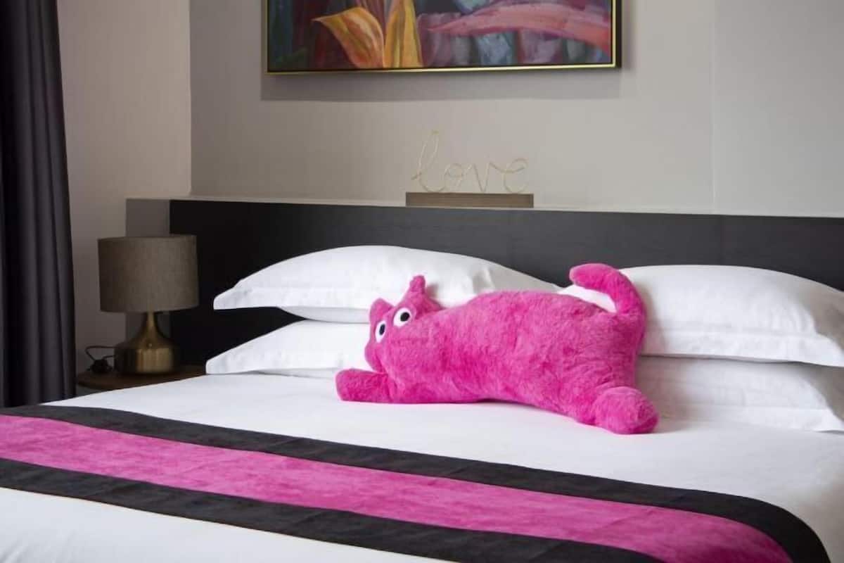 A bed with white pillows, a black headboard, a pink stuffed toy, and a lamp on the side.