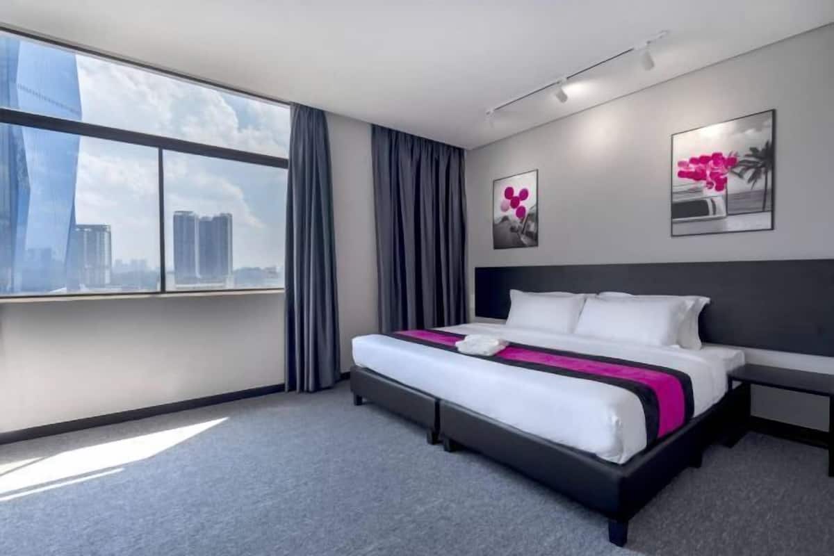 A modern hotel room with a large window, a bed, a bedside table, and artwork on the wall.