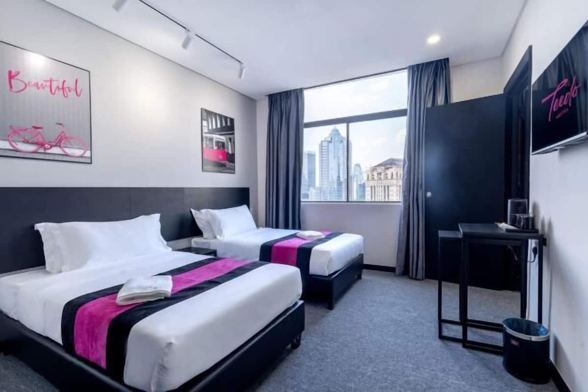 A hotel room with two beds, a desk, a chair, a TV, and a window with a city view.