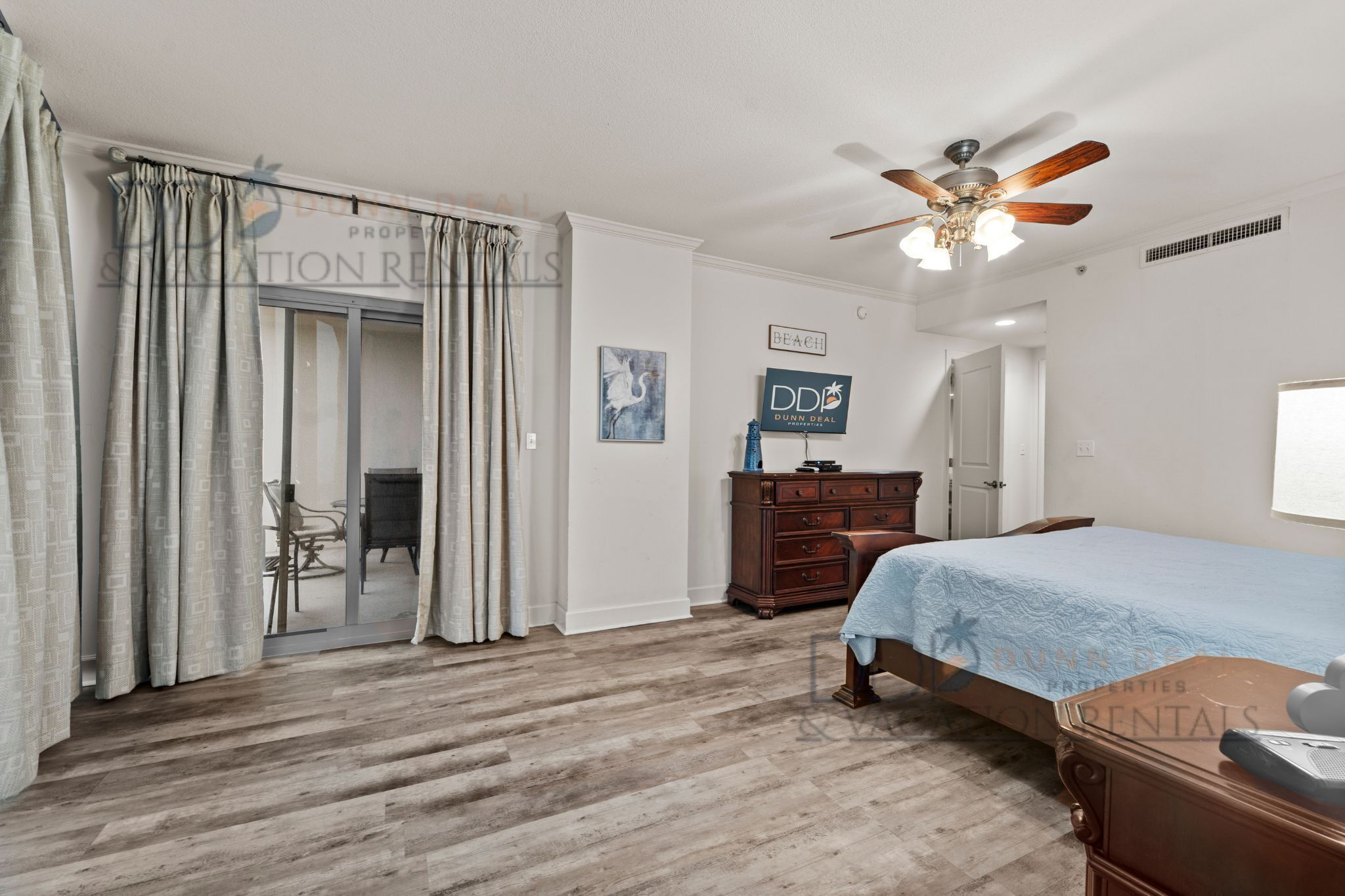 Un dormitorio con cama, cómoda, ventilador de techo y puerta que da a un balcón.